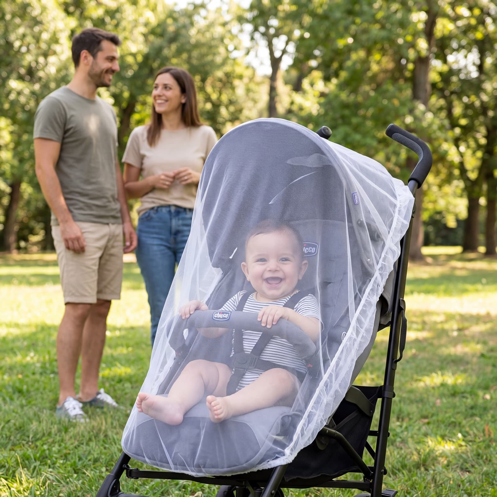 A laughing baby in a buggy under the Mosticare Bambino Carello mosquito net, parents standing together in a sunny park.