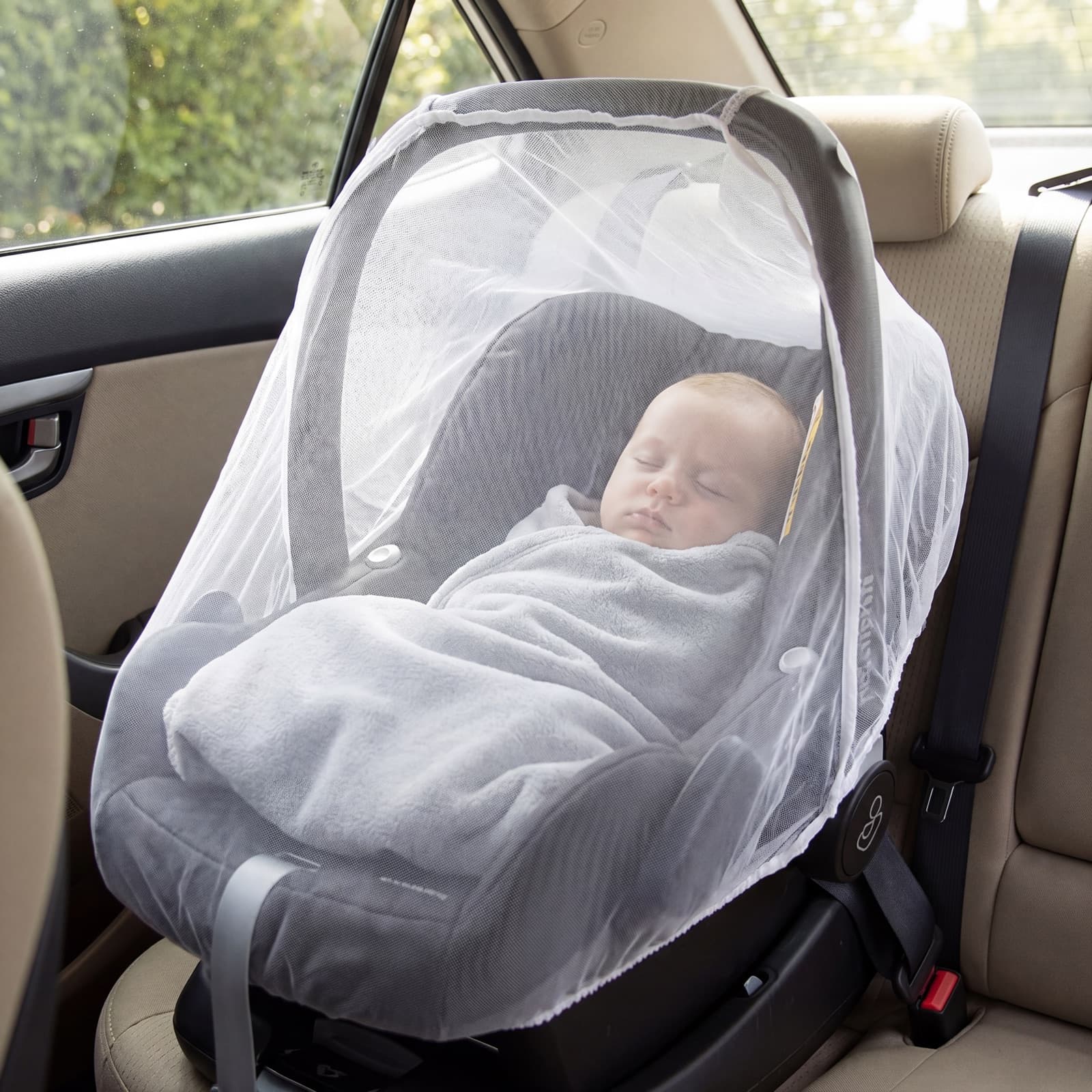 A swaddled newborn sleeping in a rear-facing car-seat carrier under the Mosticare Bambino Carello mosquito net.