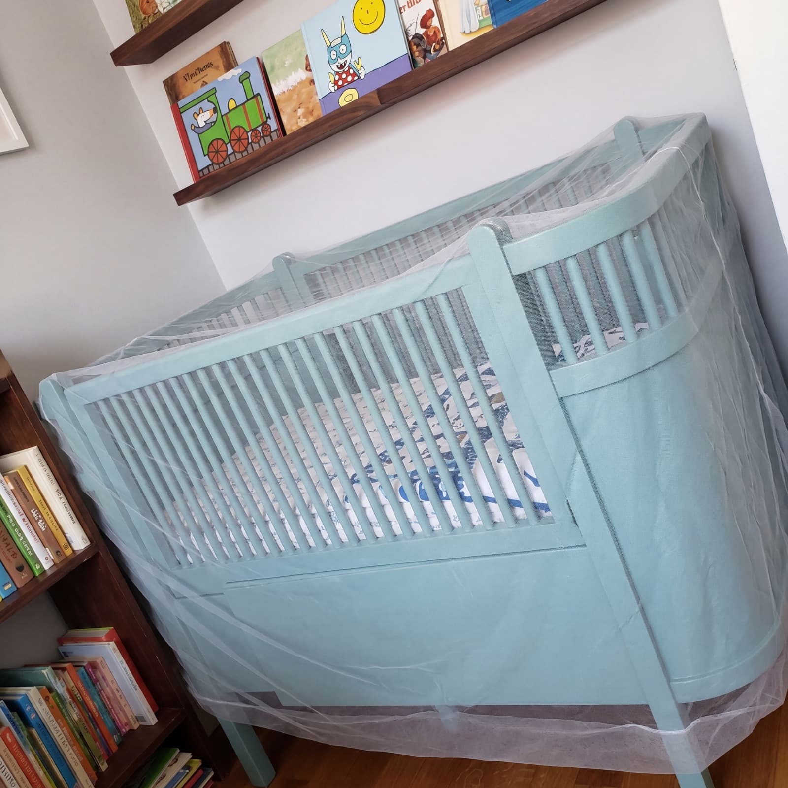 The Mosticare Bambino Dorme mosquito net draped over a baby's cot in a sunlit nursery.