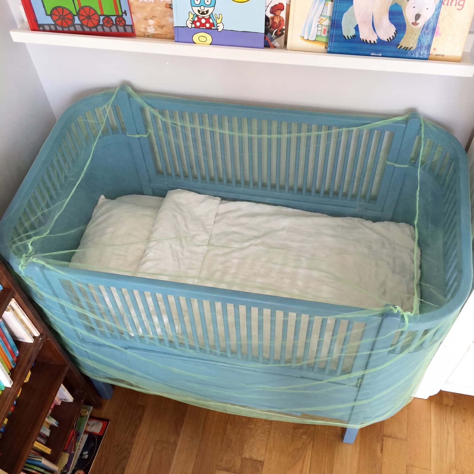 Overhead view of the Mosticare Bambino Dorme net covering a cot with bedding inside.