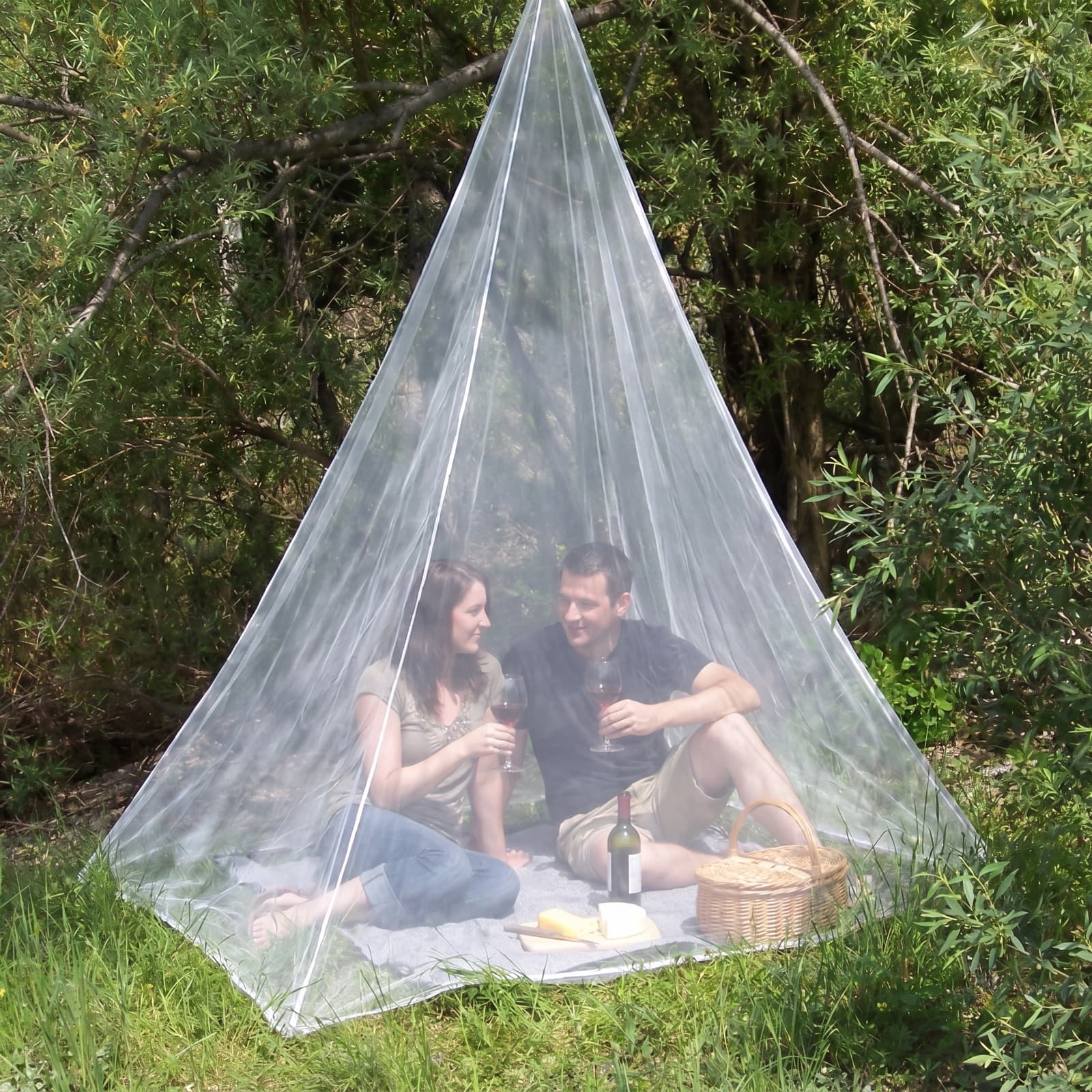 A couple enjoying a picnic under the Mosticare Traccia travel mosquito net in a woodland clearing.