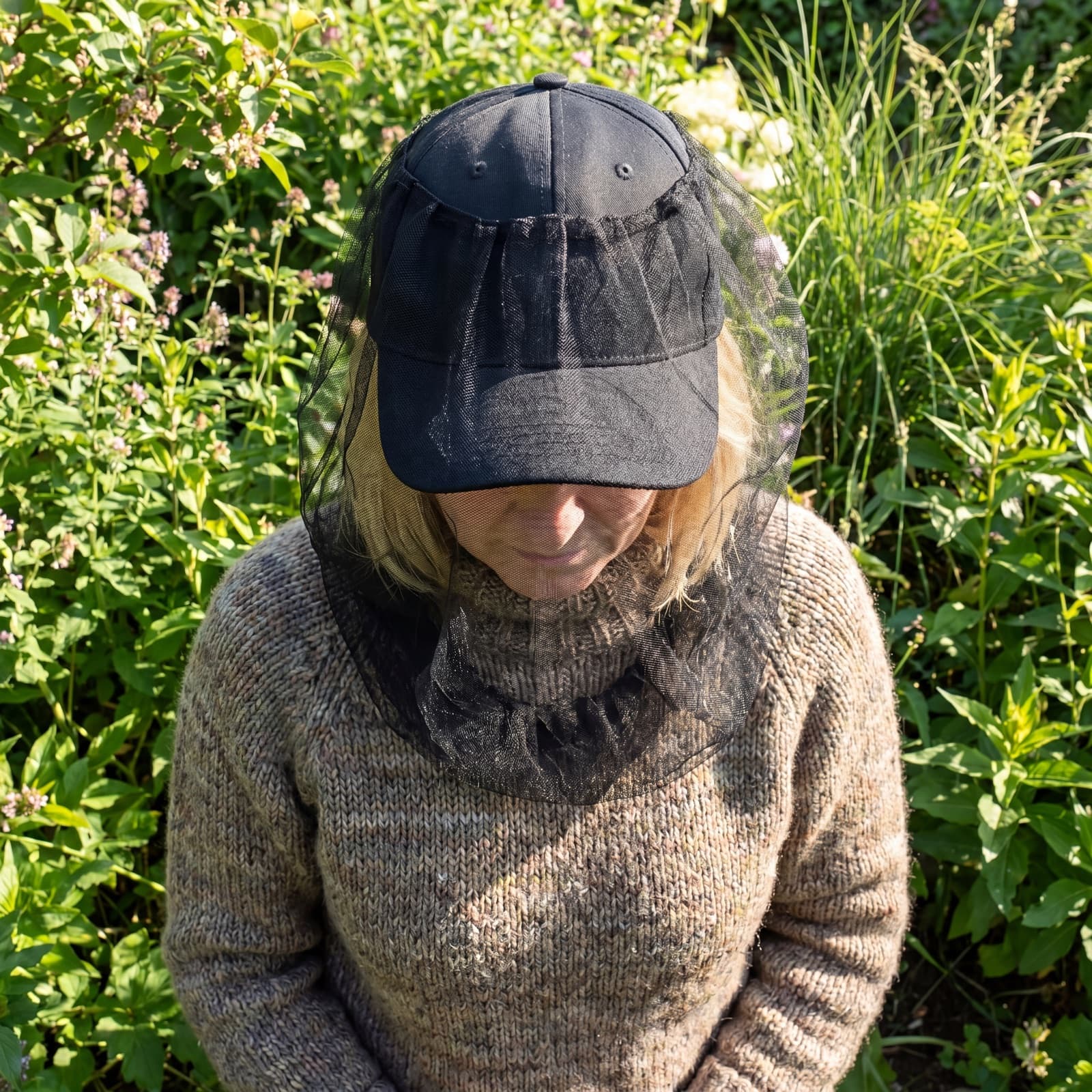 A woman in a garden wearing the Mosticare Volto head net hanging from a cap over her face.