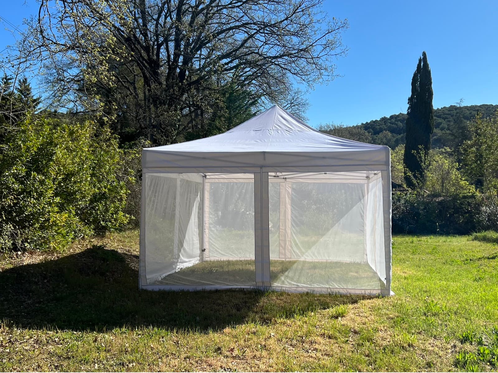 The Mosticare Terrazza mosquito-net gazebo with mesh walls set up on a sunlit garden lawn.